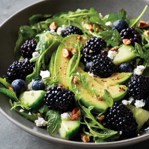 A bowl of salad with greens, nuts, and blueberries.