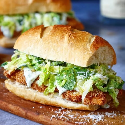 A sandwich with lettuce and fish on a wooden table.